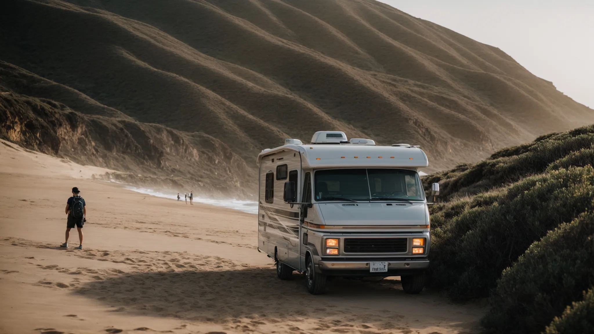 an rv parked near the beach with surfers catching waves as hikers explore trails in the nearby hills.